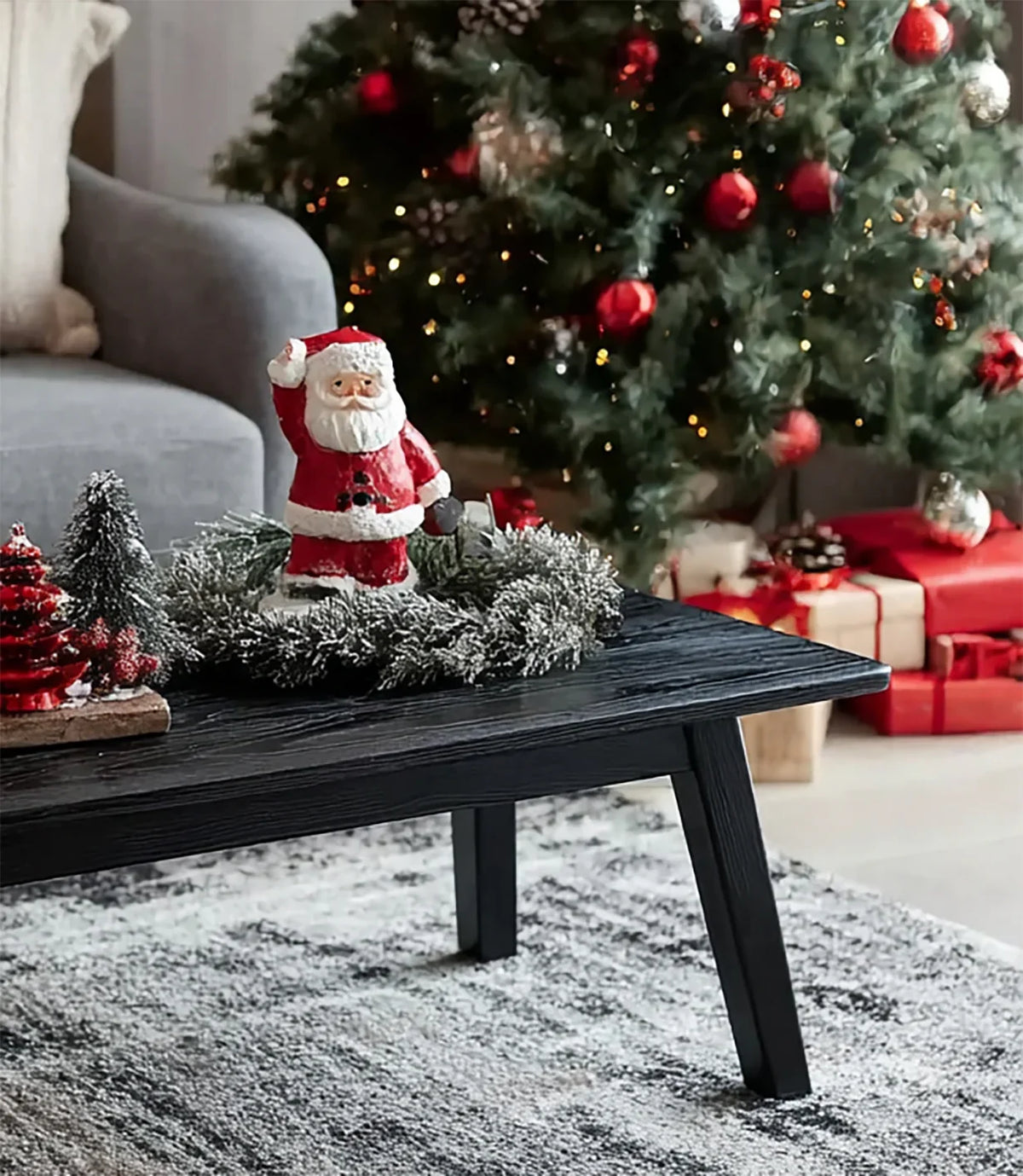 Christmas living room with decorated tree, red gifts, and Santa figurine on black coffee table