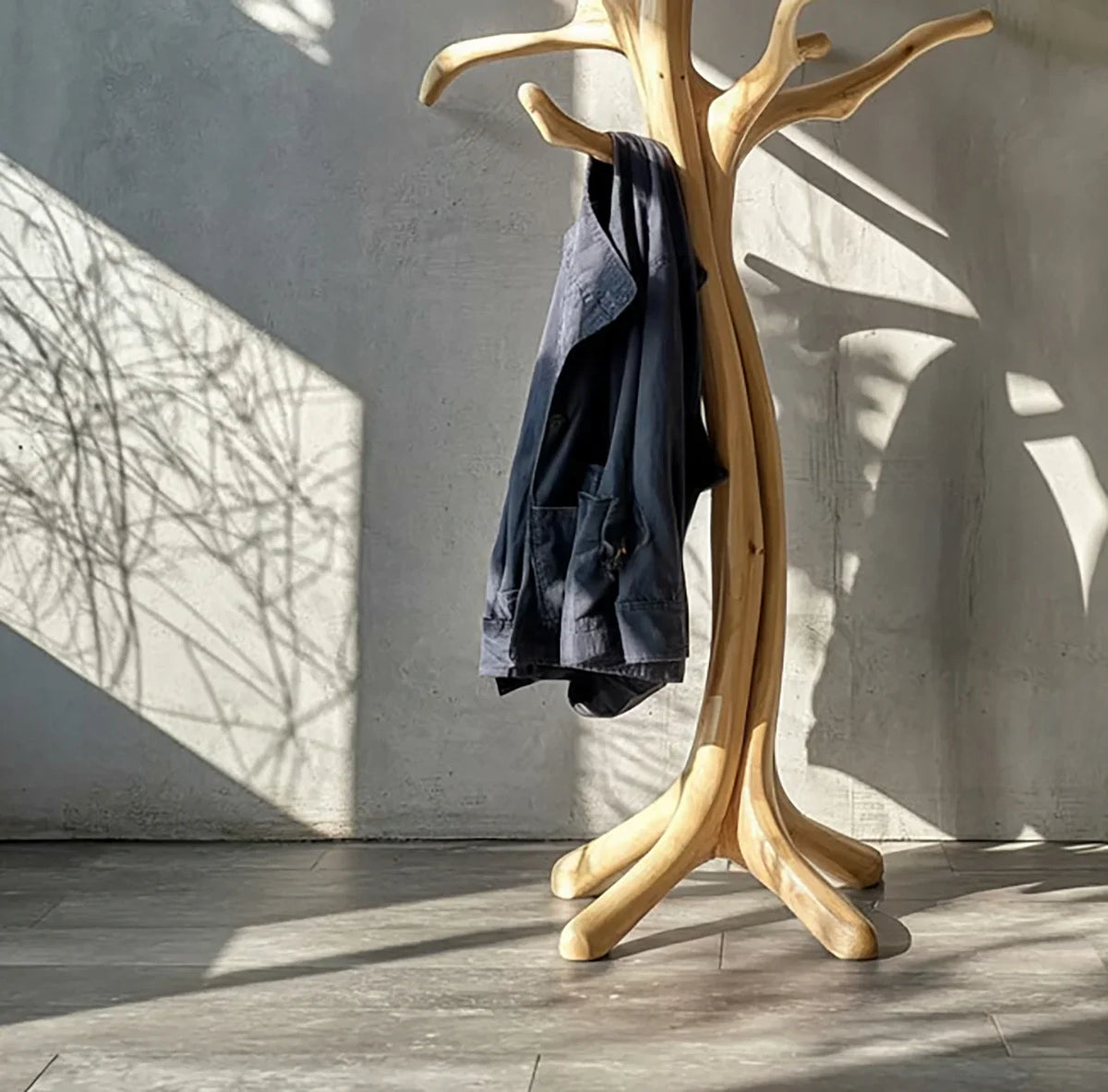 Natural wood tree-shaped coat rack with jacket, modern minimalist interior, sunlight shadows