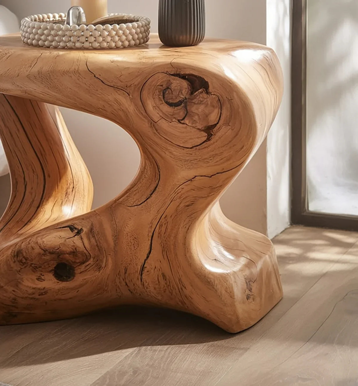 Close-up of a smooth wooden table with natural knots and curved design on light hardwood floor by window