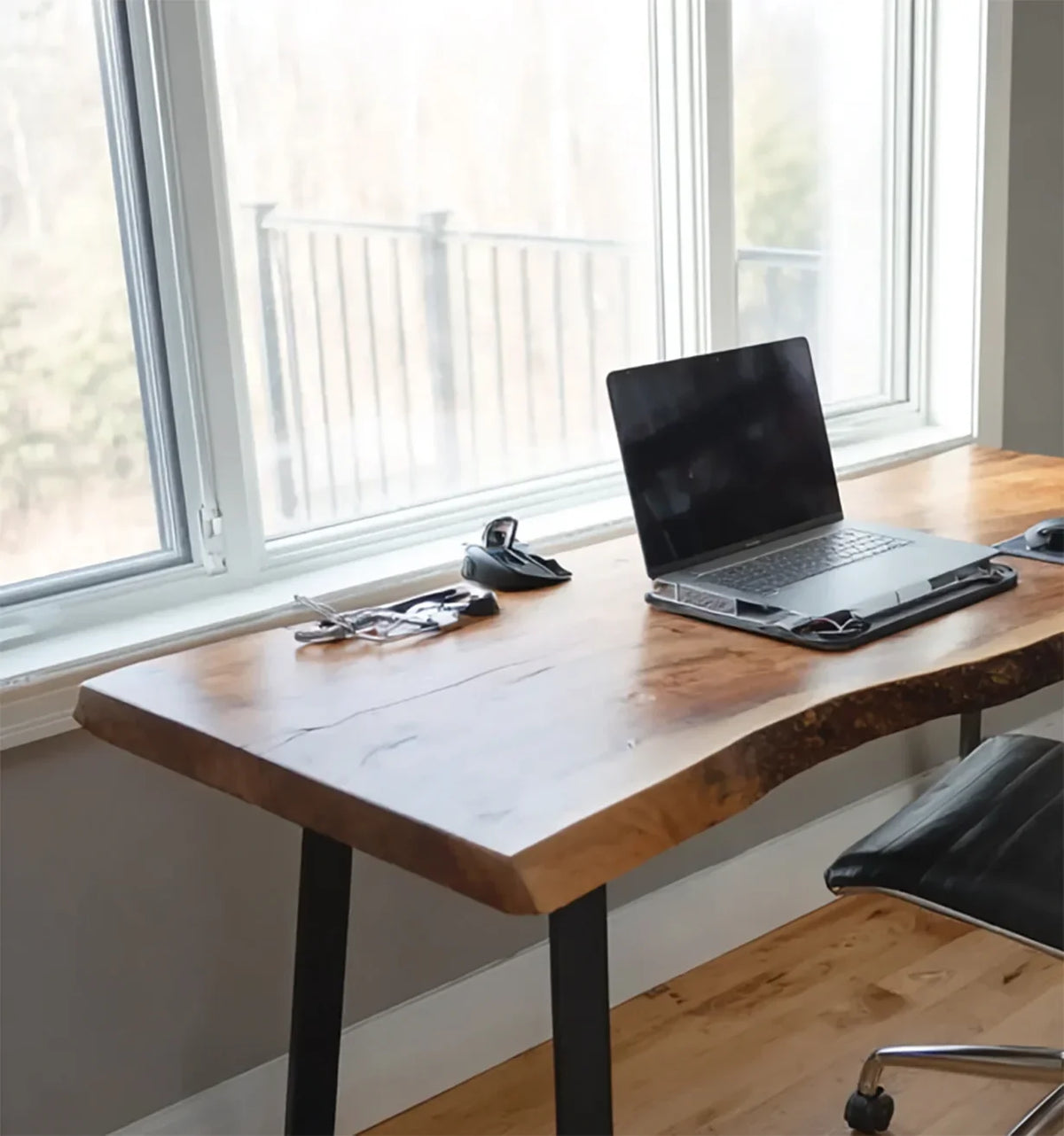 Wooden desk with live edge by large window, laptop on stand, office chair, and accessories