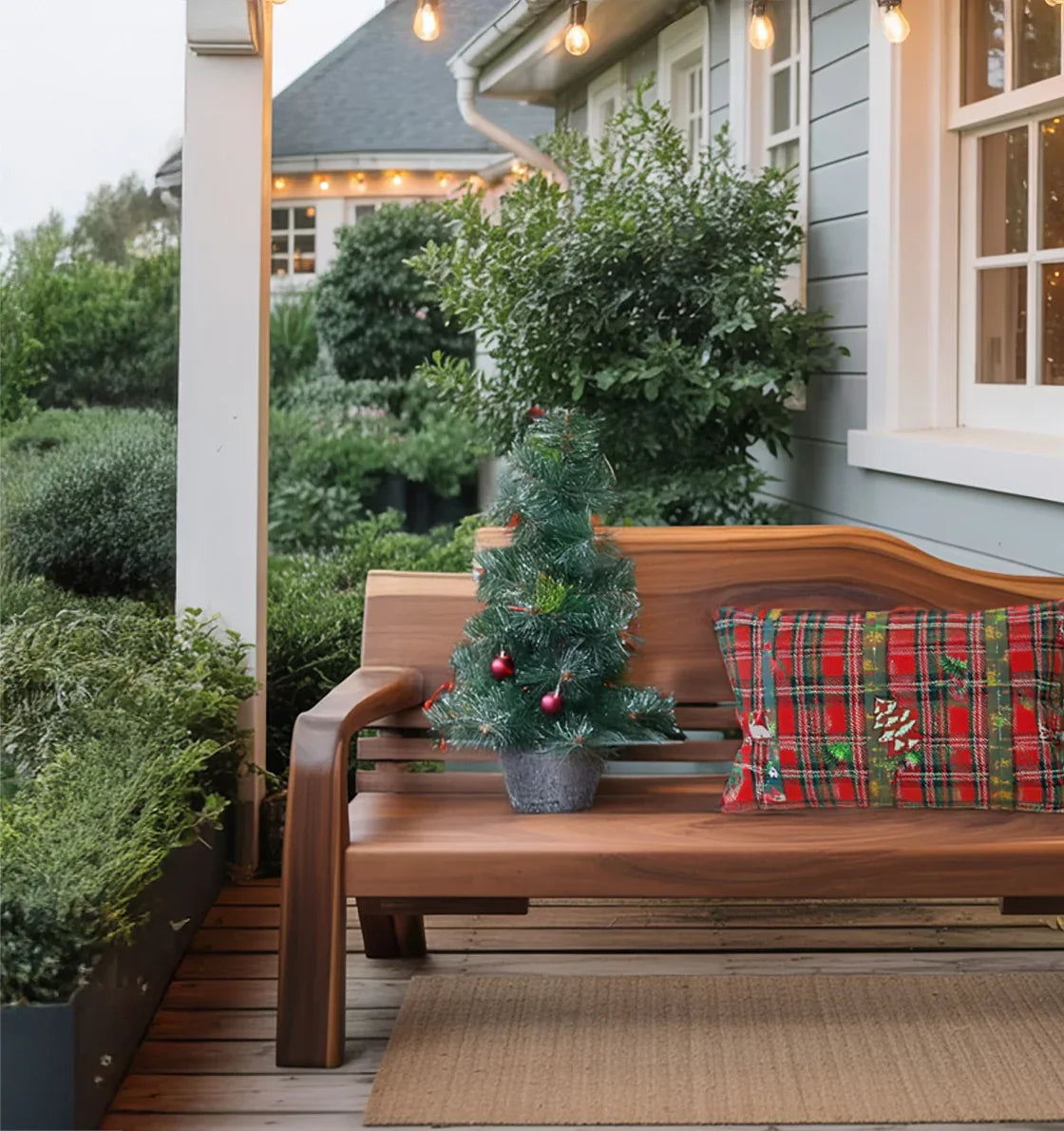 Cozy porch with wooden bench, small decorated Christmas tree in pot, and red plaid holiday pillow