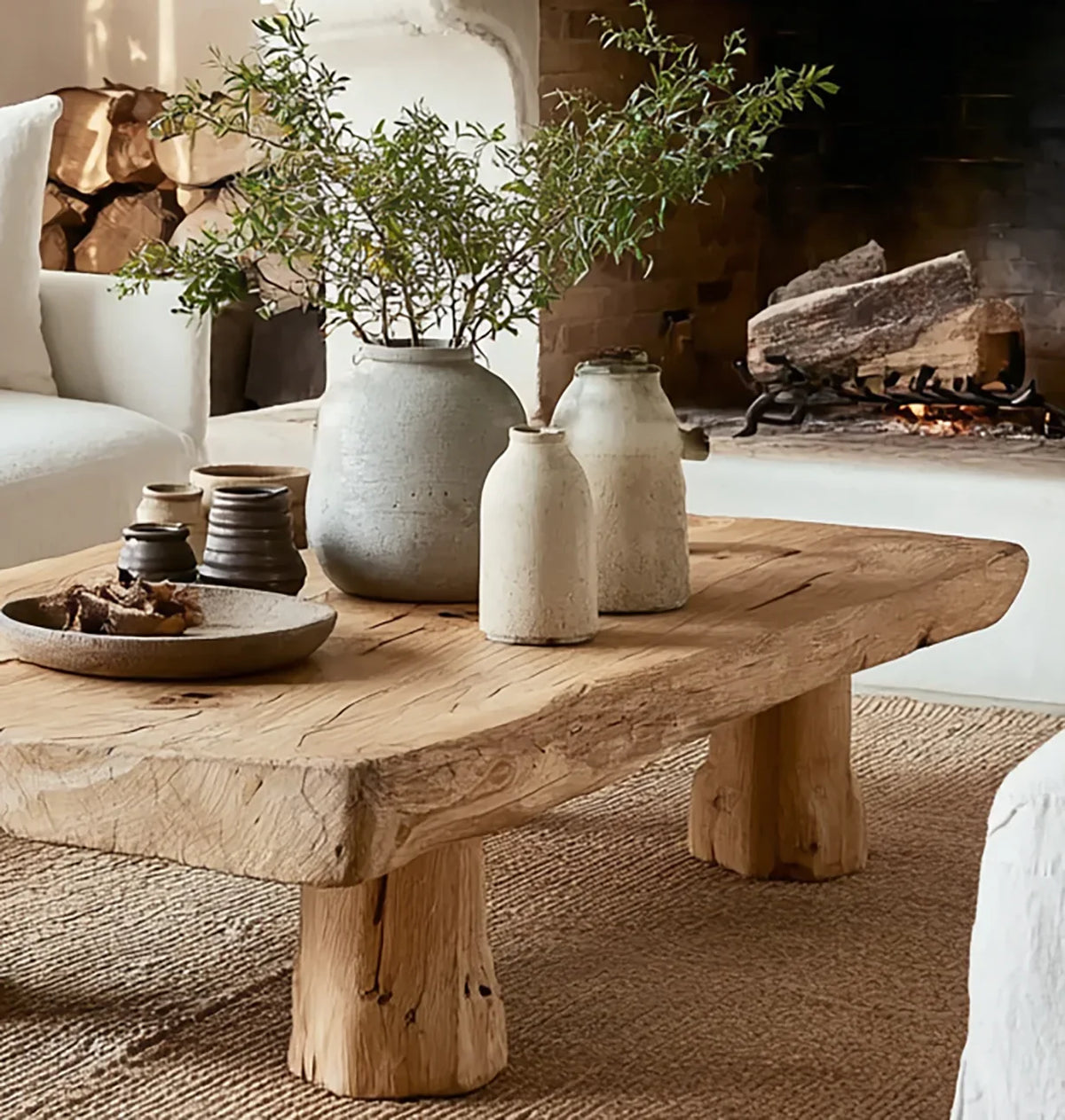 Rustic solid wood live edge coffee table with ceramic vases in cozy living room by fireplace