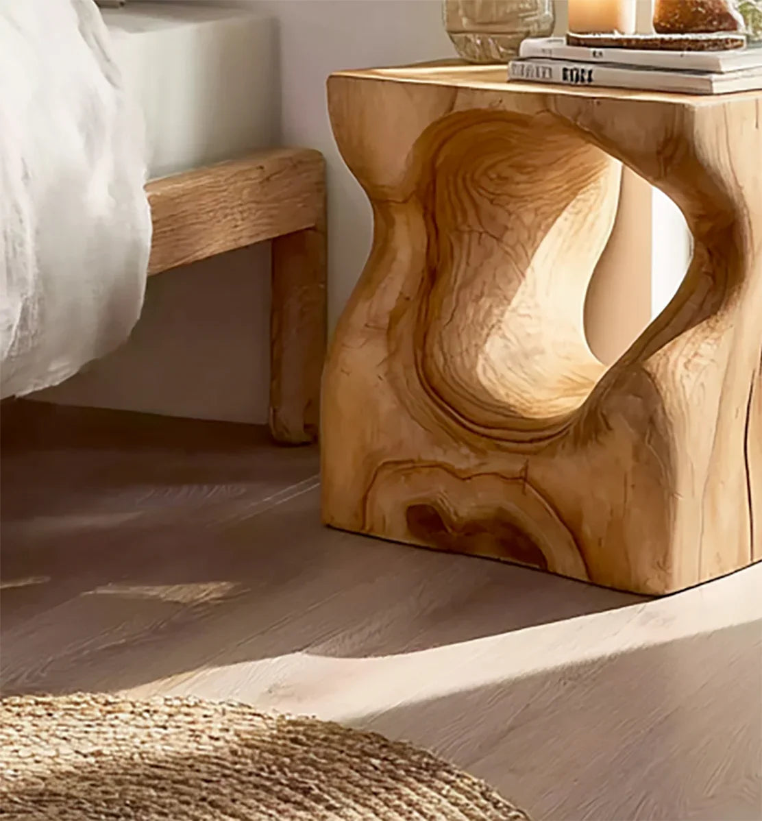 Modern wooden side table with unique carved design beside wooden bed frame in bright bedroom