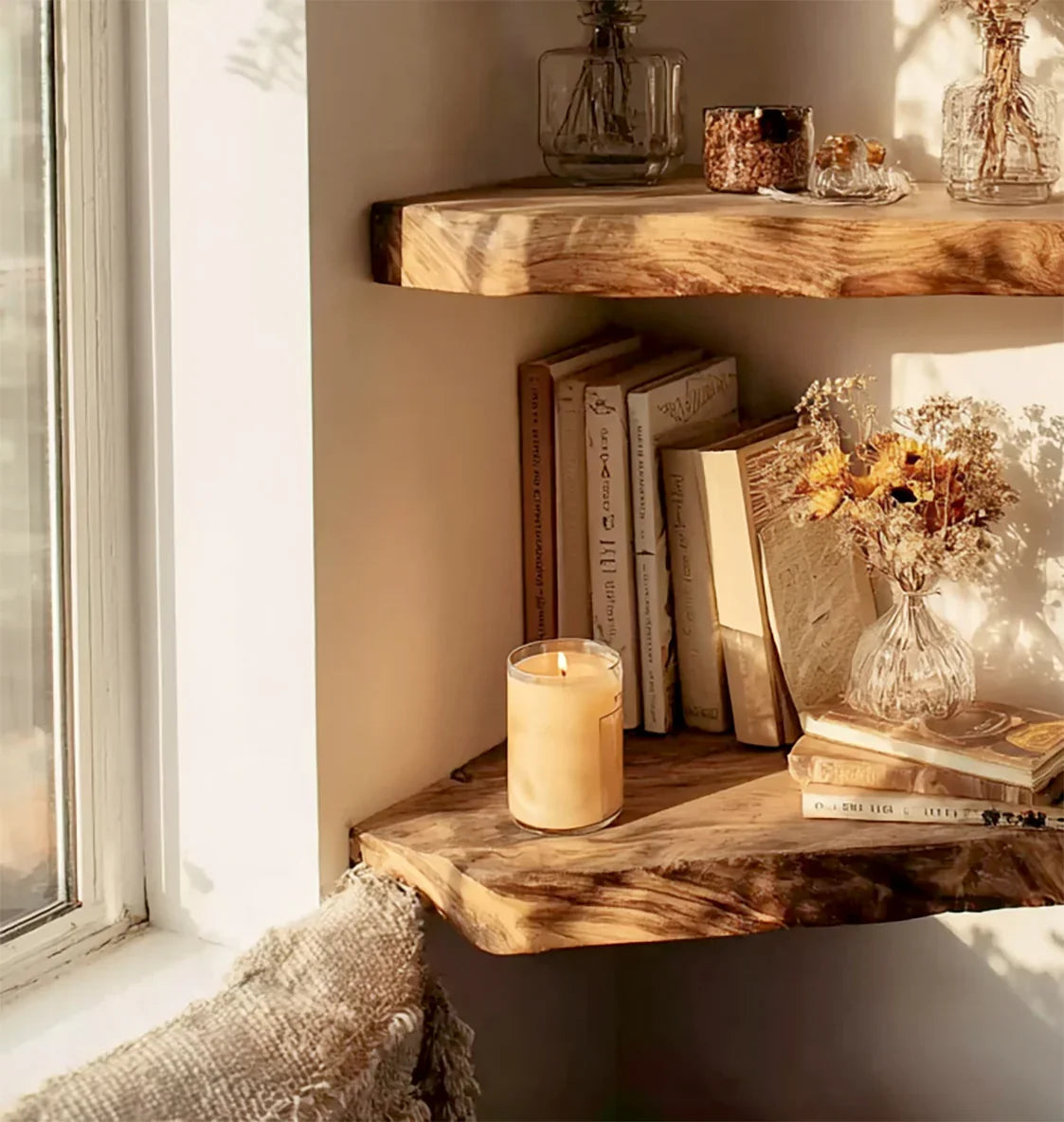 Rustic wooden corner shelves with dried flowers in glass vase, books, and lit candle by window