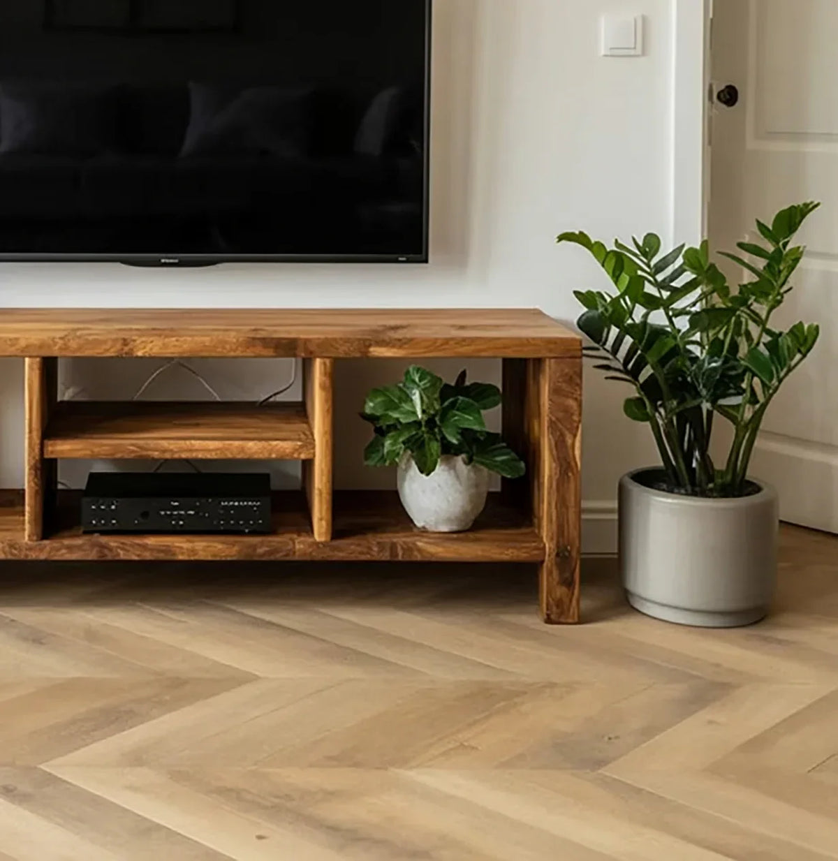 Modern living room with wooden TV stand, flat screen TV, potted plants, and chevron wood flooring