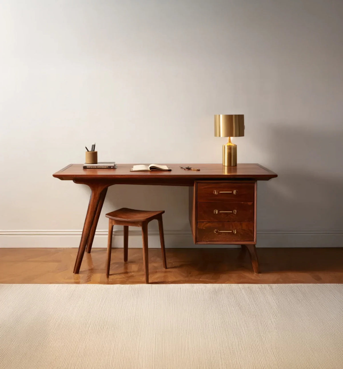 Mid-century modern wooden desk with three drawers, matching stool, gold lamp, and office accessories