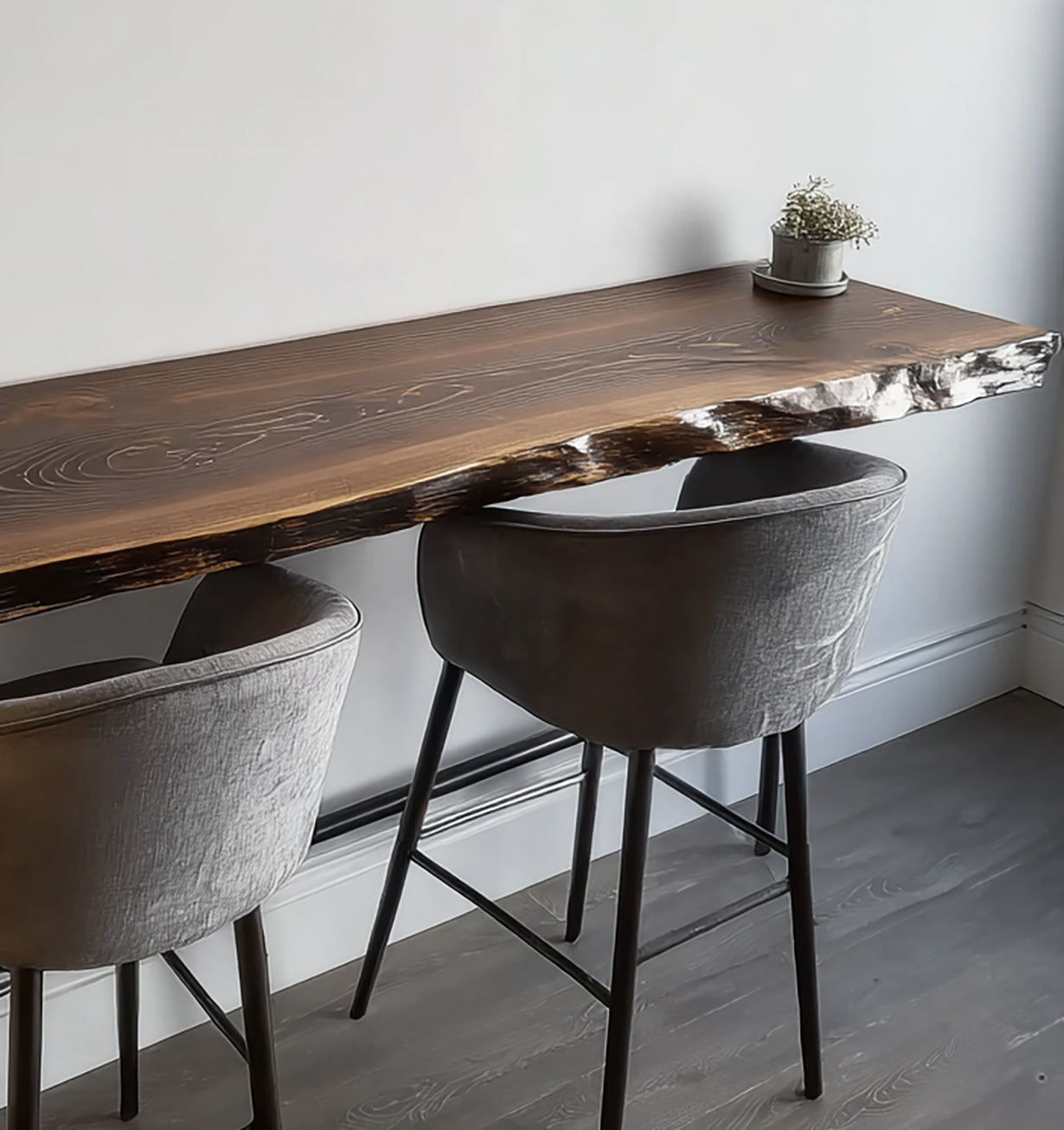 Live edge wooden bar table with two gray upholstered stools and small potted plant