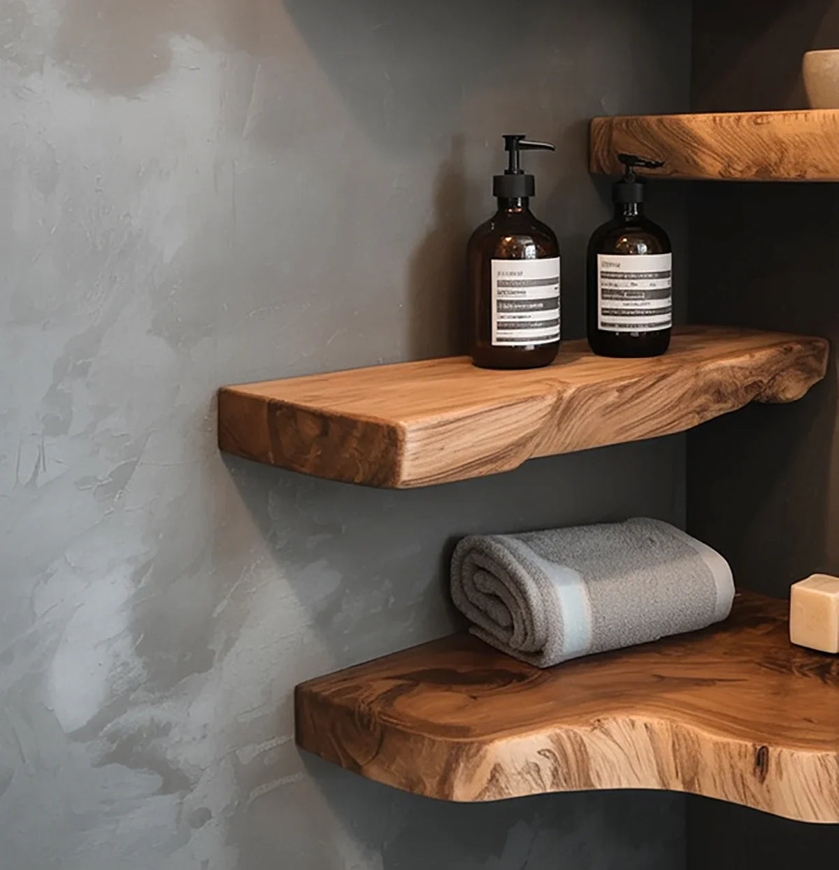 Two amber pump bottles and a folded gray towel on rustic live edge wooden shelves against gray textured wall