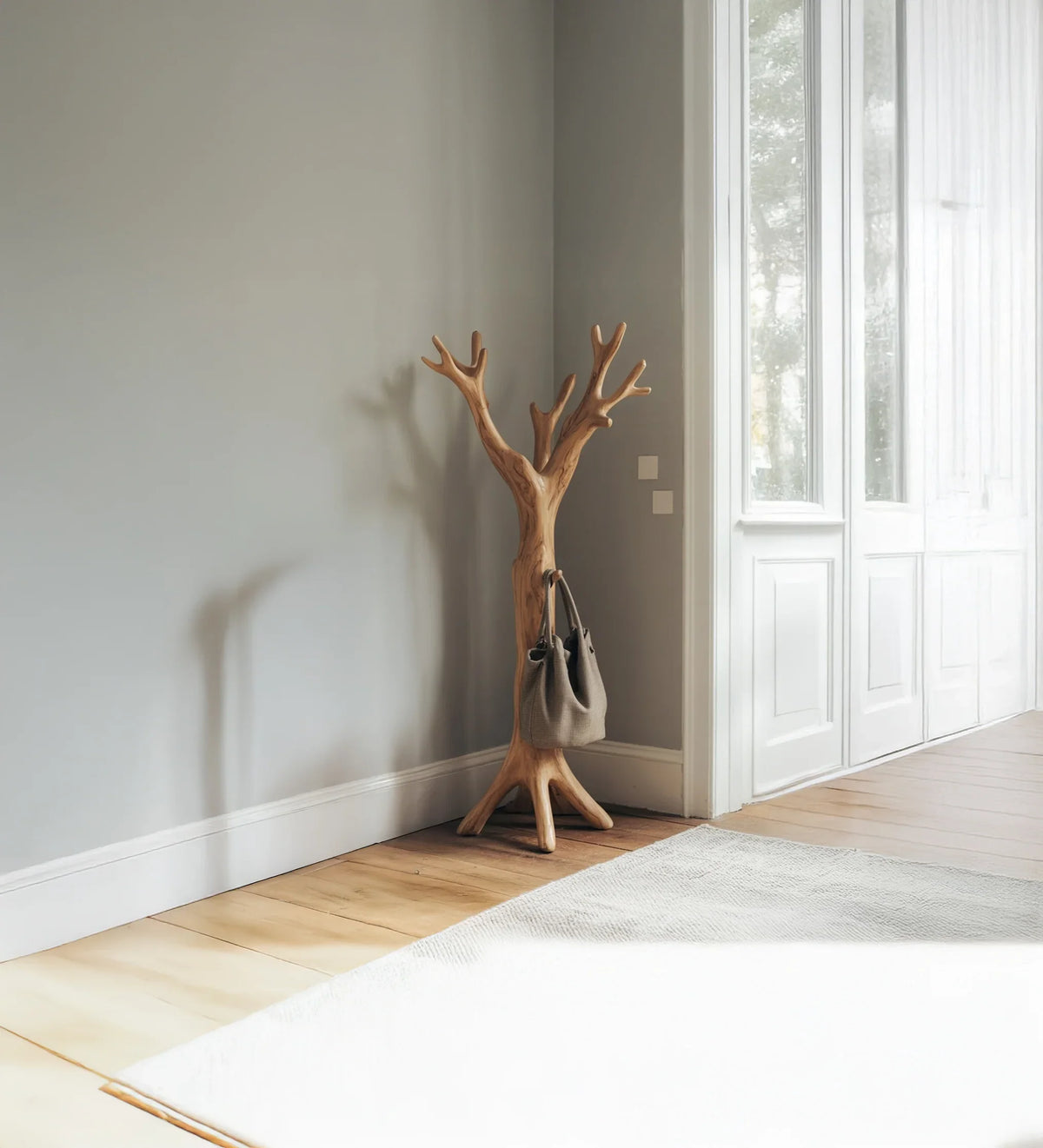 Minimalist interior with wooden tree-shaped coat rack holding a gray bag by white doors