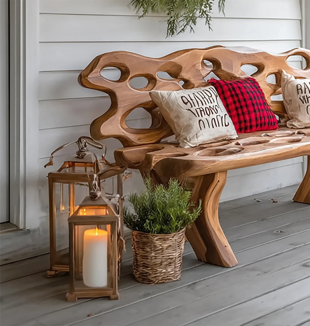 Carved wooden bench with decorative pillows on a porch with candles and potted plant
