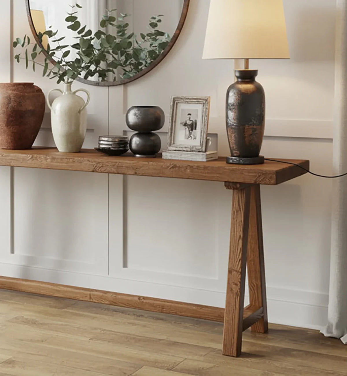 Wooden console table with decorative vases, a table lamp, framed photo, and round mirror in modern interior