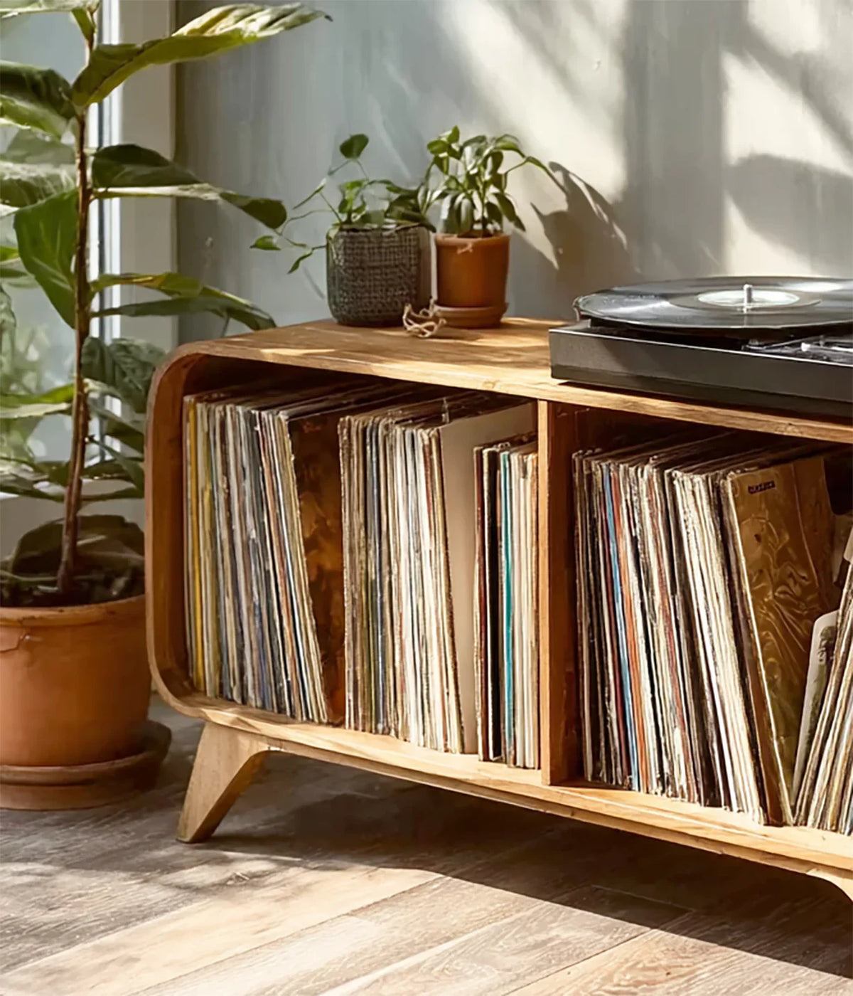 Mid-century wooden record player stand with vinyl collection and potted plants in sunlit room