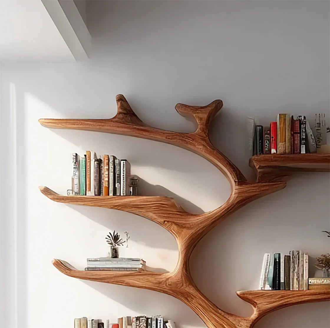 Wooden branch-shaped bookshelf mounted on white wall holding books and small decor