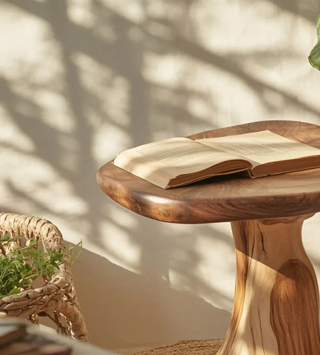 Open book on round wooden side table with woven basket and plant in bright natural light