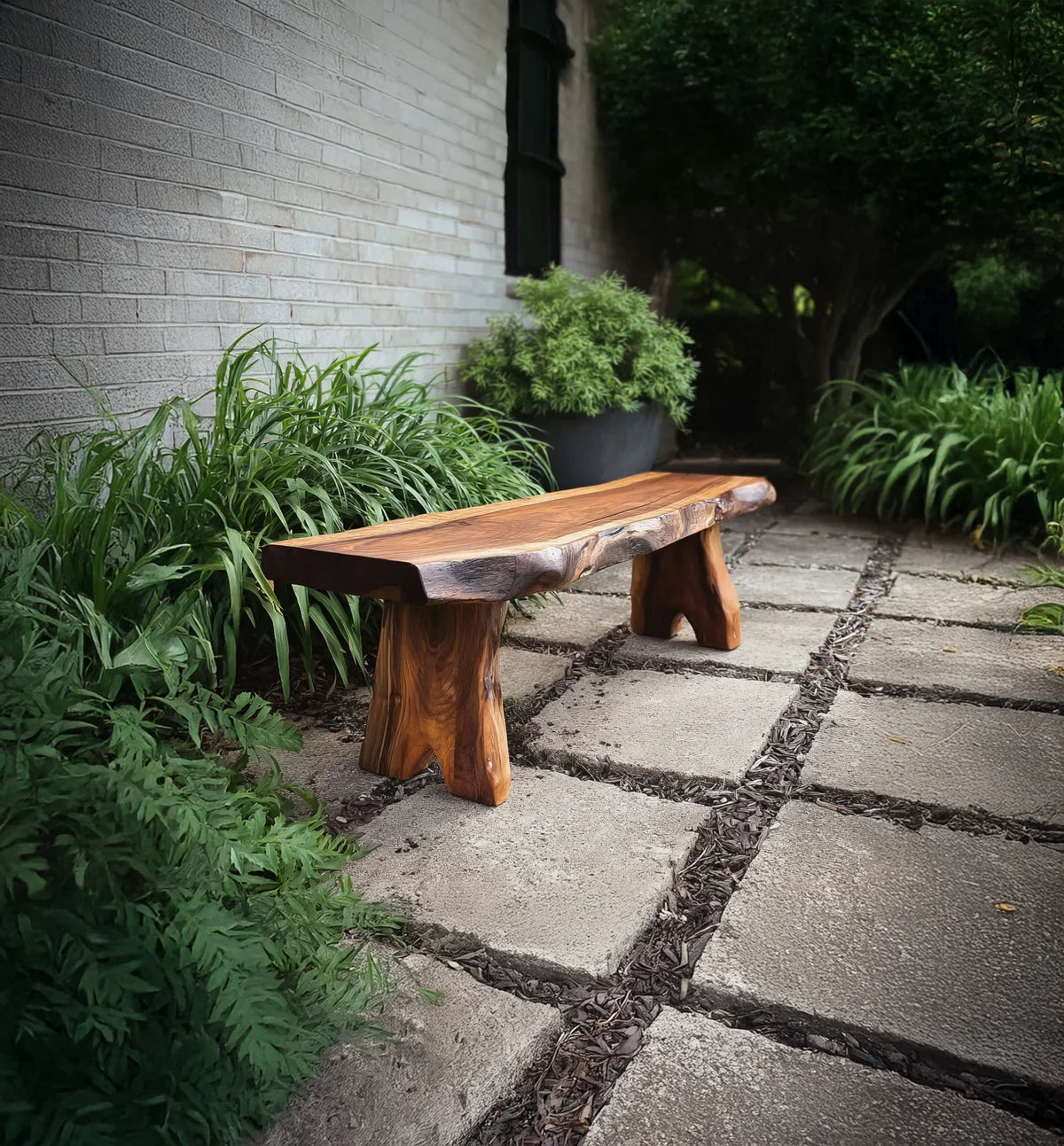 Handcrafted wooden bench on stone patio surrounded by green plants and white brick wall