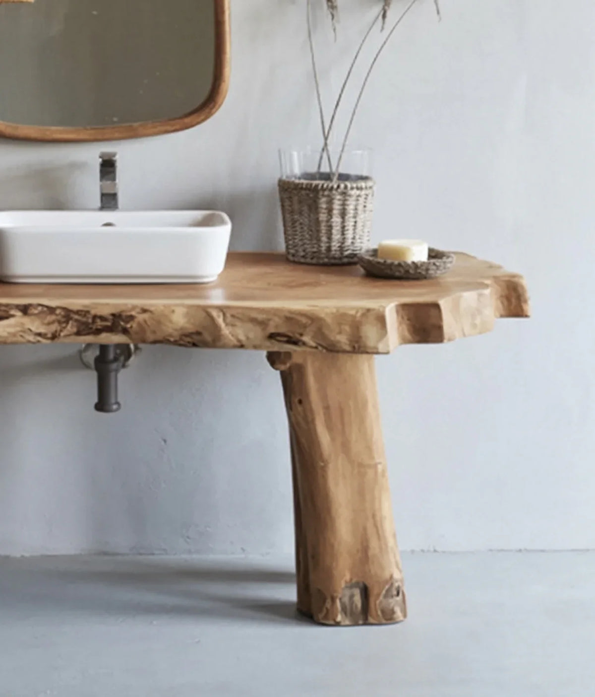 Rustic wooden bathroom vanity with white rectangular sink, wicker vase, and candle on concrete floor