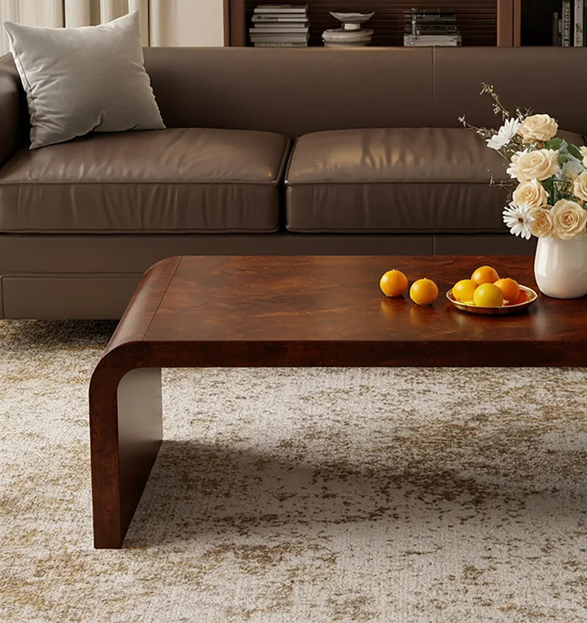 Modern brown leather sofa with gray pillow, wooden coffee table with oranges, and floral vase on textured rug