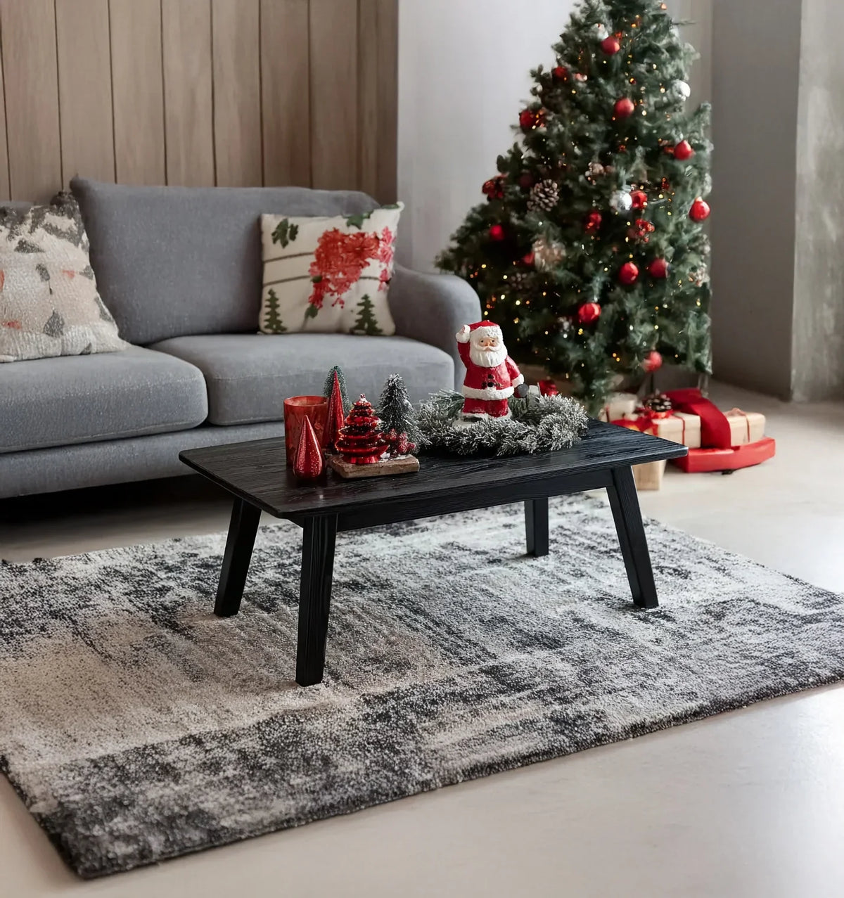 Cozy living room with gray sofa, Christmas tree with red ornaments, and decorated black coffee table