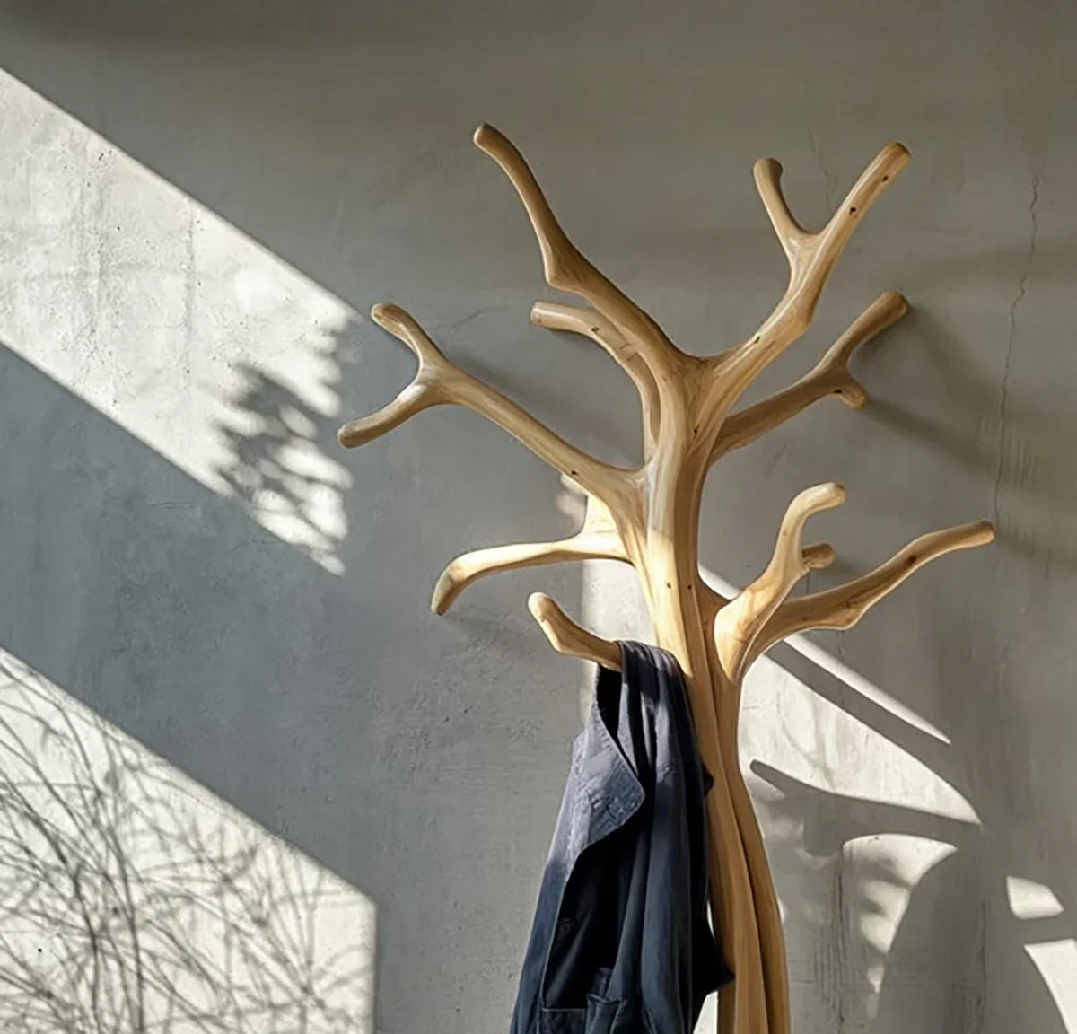 Solid wood tree coat rack with natural branches against gray wall, blue jacket hanging