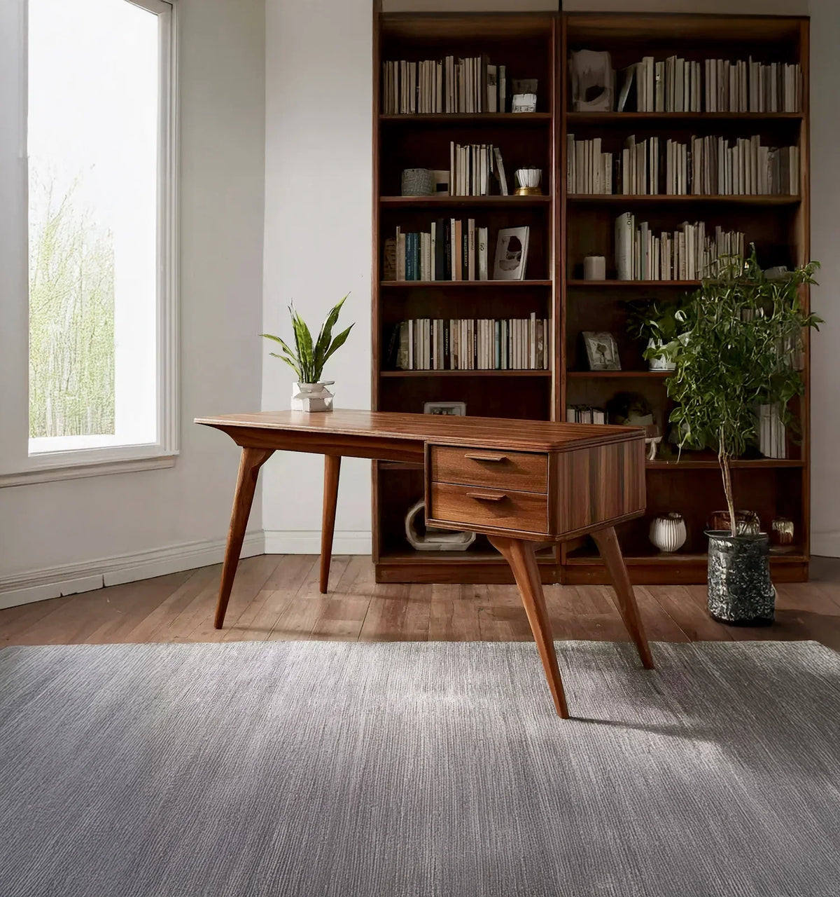 mid-century modern wooden office desk with drawers, potted plants, bookshelf filled with books in a bright room