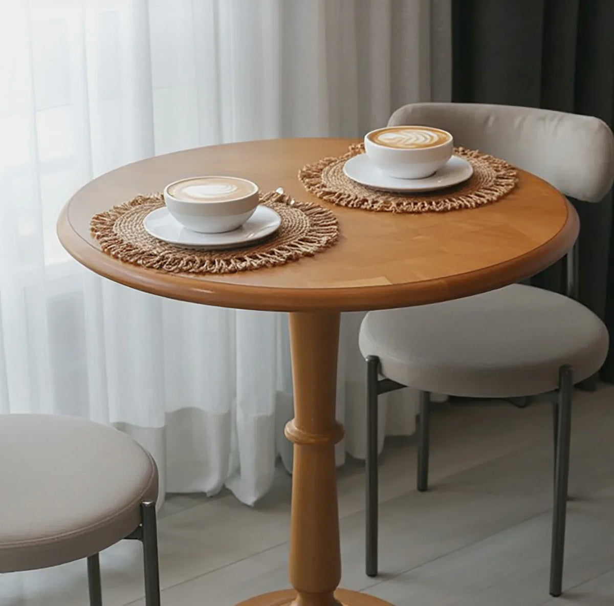 Round solid wood table with two modern chairs, featuring lattes on woven placemats