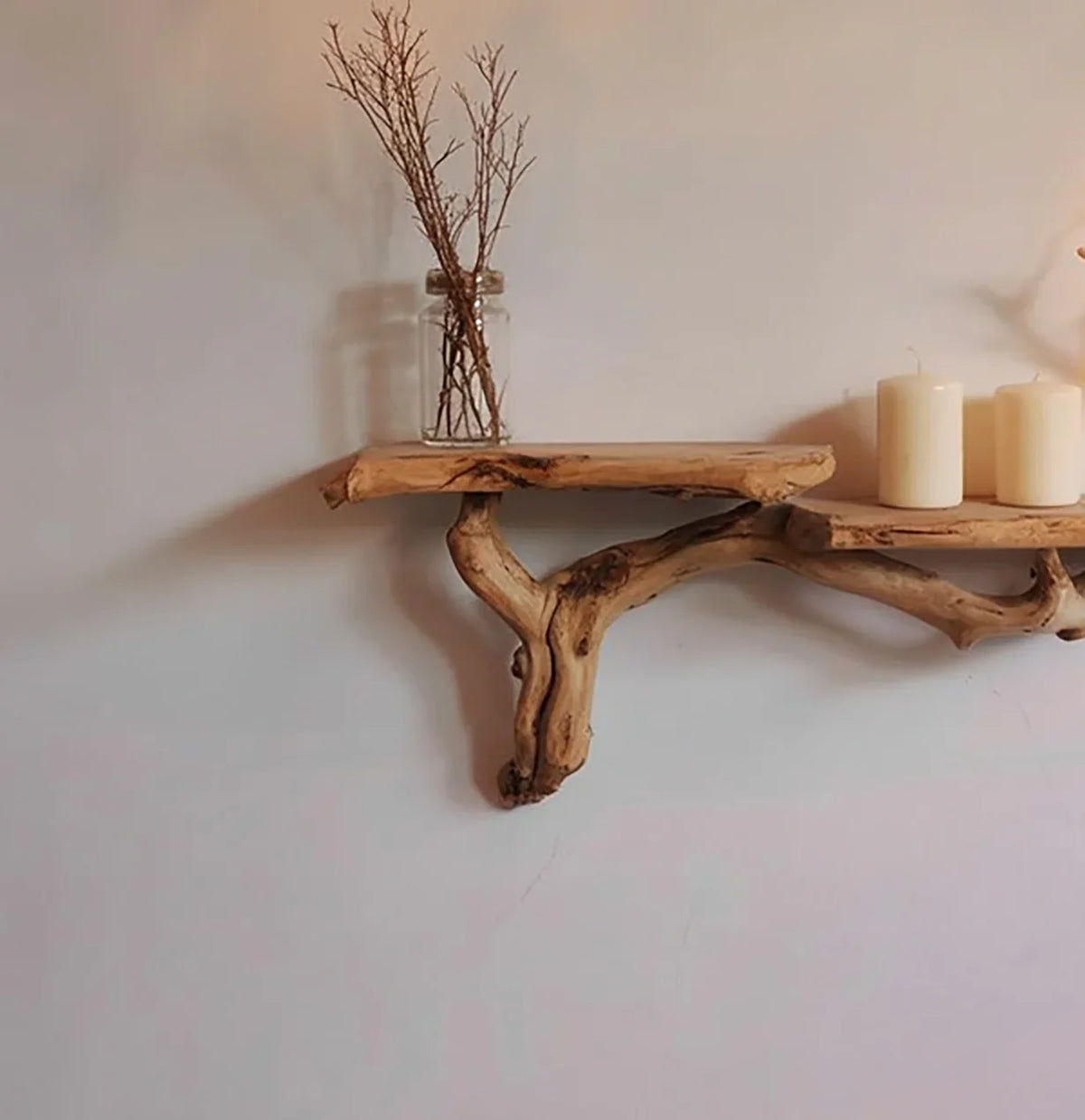 Live edge solid wood floating shelf with natural branch support, decorated with candles and vase