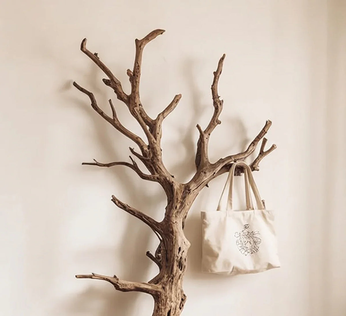 Live edge tree branch coat rack with canvas tote bag against beige wall