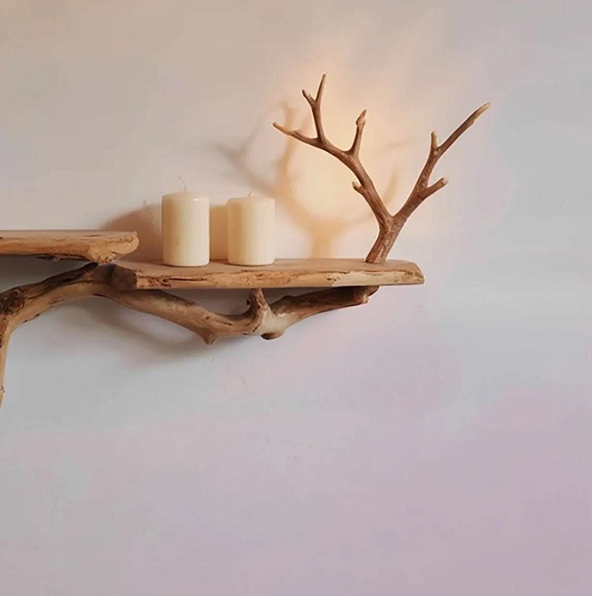 Live edge wooden floating shelf with branch accents and two pillar candles on a light wall