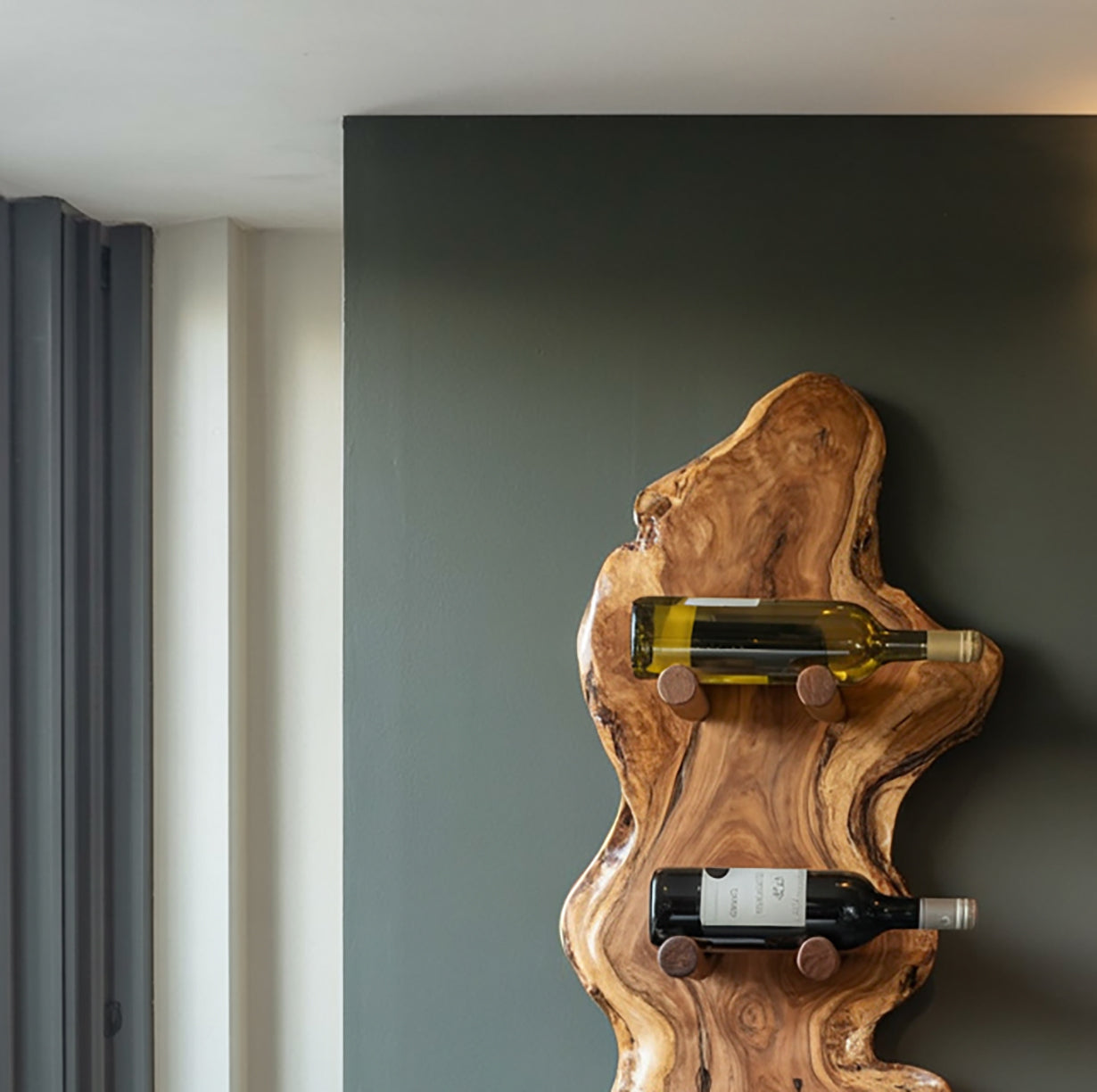 Rustic live edge wooden wine rack mounted on dark wall holding two wine bottles