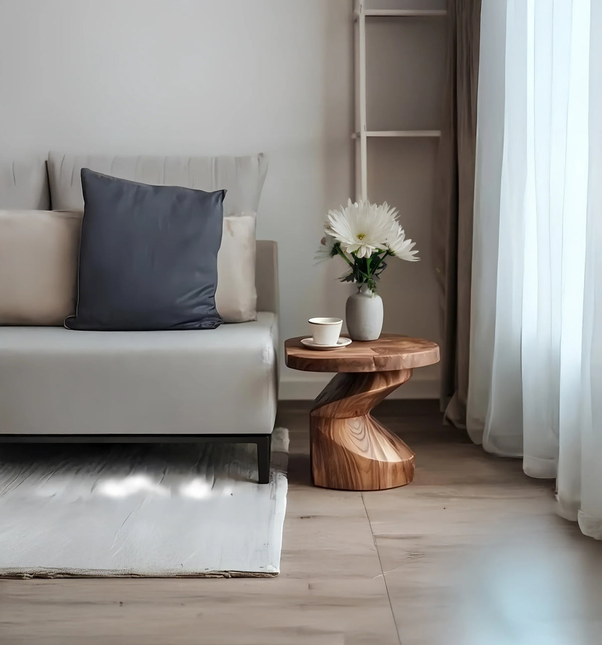Modern living room corner with a gray sofa, black pillow, wooden side table, white flowers, and cup