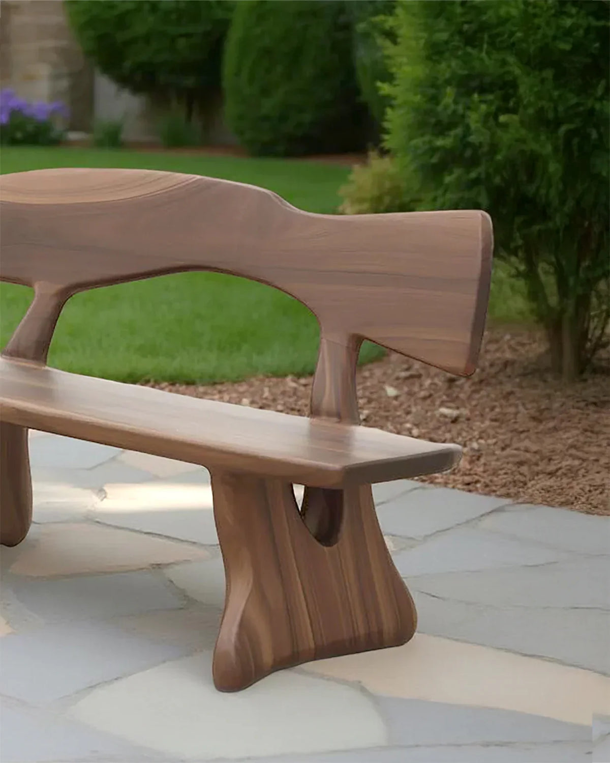 Modern wooden outdoor bench with sculpted design on stone patio near green garden