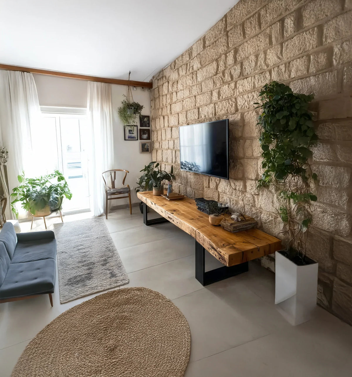 Modern living room with stone wall, wall-mounted TV, wooden console, indoor plants and natural light