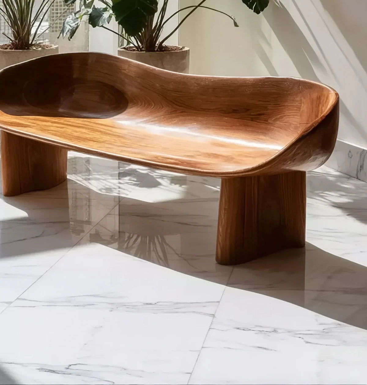 Modern carved wooden bench with smooth organic curves on white marble floor in sunlit room