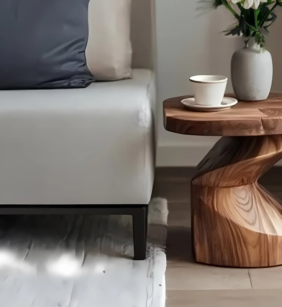 Modern living room corner with beige sofa, blue-grey pillow, wooden side table, ceramic cup, and vase with flowers