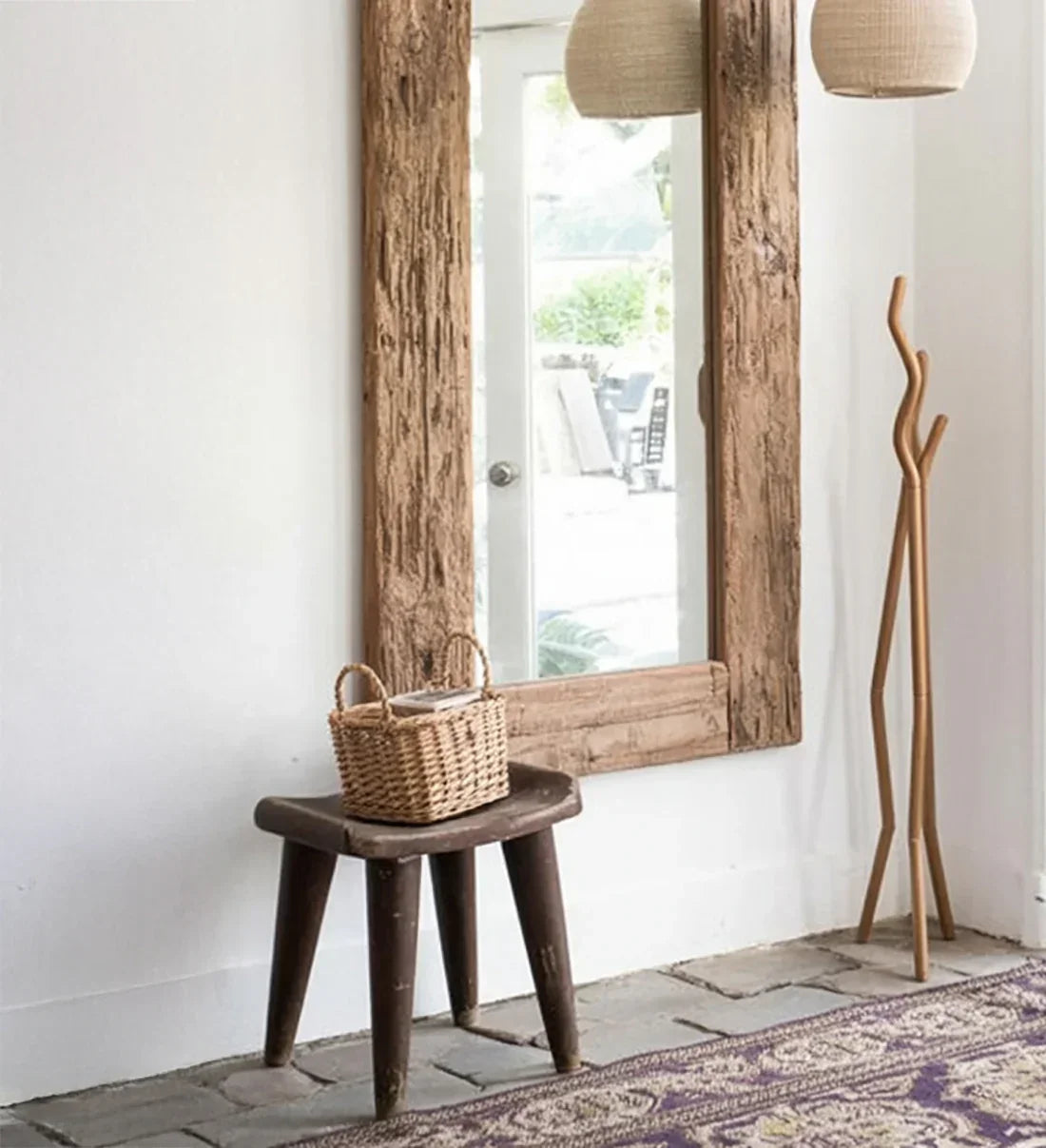 Rustic wood framed mirror, wooden stool with wicker basket, and coat rack in bright entryway