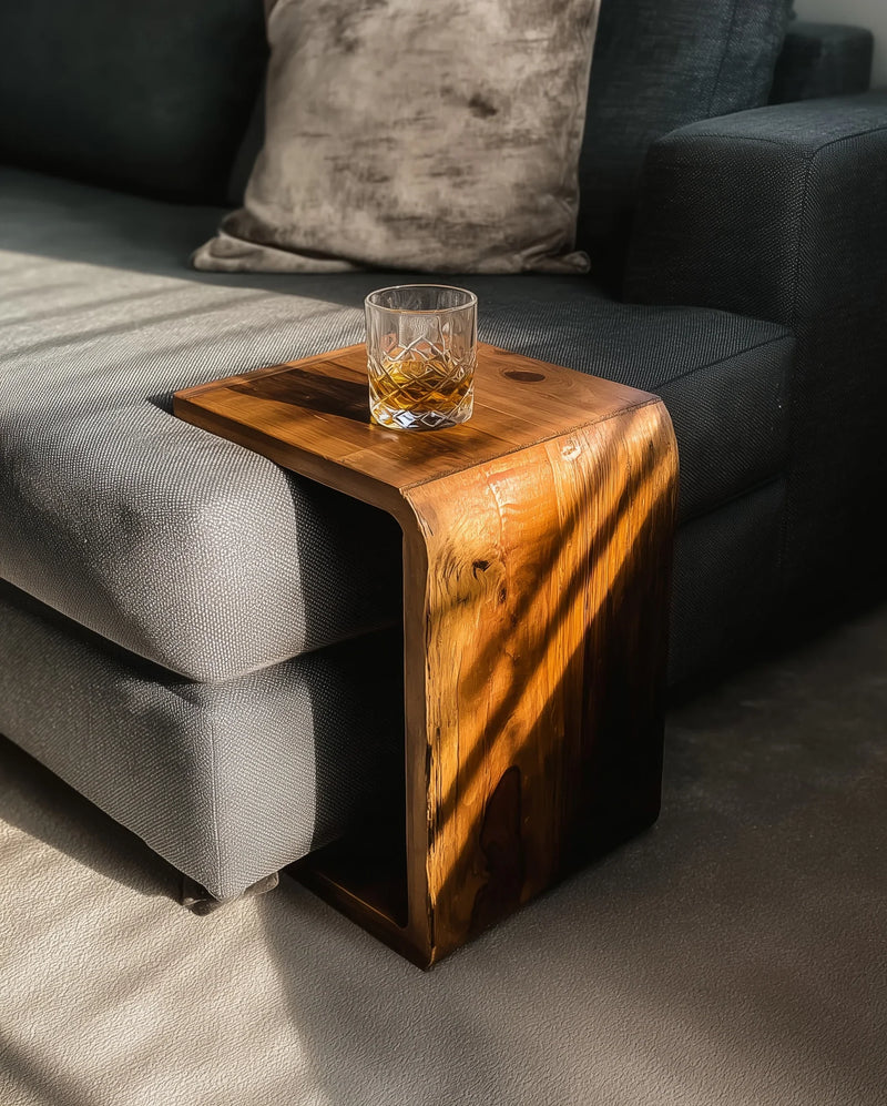 Modern living room with gray fabric sofa, plush pillow, wooden side table, and glass of whiskey