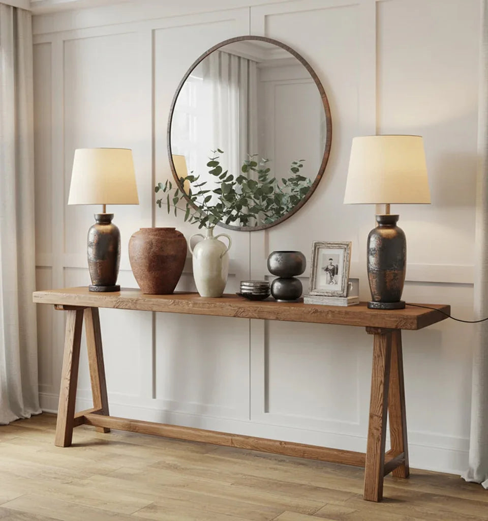 Rustic wooden console table with decorative vases, framed photo, lamps, and round wall mirror