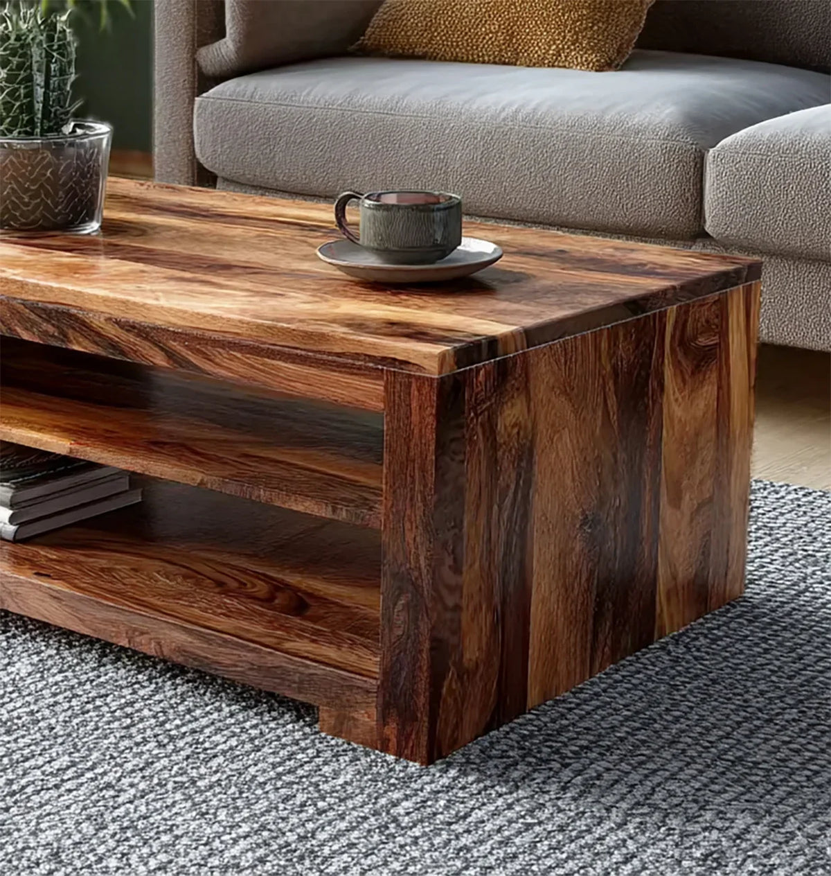 Wooden coffee table with rich grain and open shelf, dark ceramic cup and saucer on top, gray textured sofa background