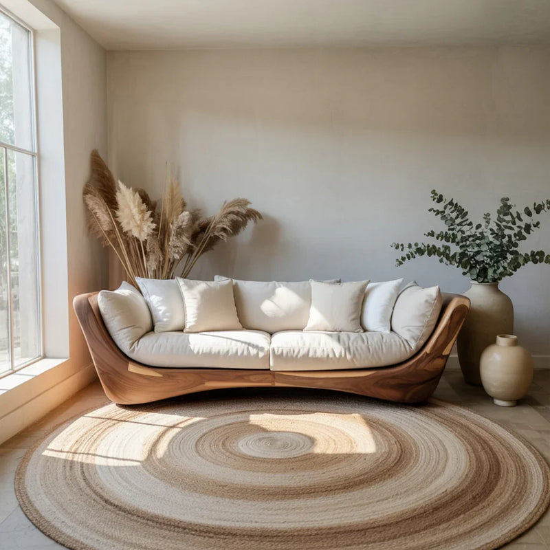 Modern curved wooden sofa with white cushions in sunlit neutral living room with pampas grass and vases