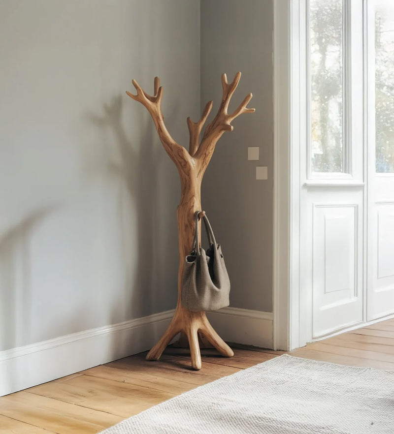Wooden tree-shaped coat rack with a gray bag in a bright room with wooden floor and white door