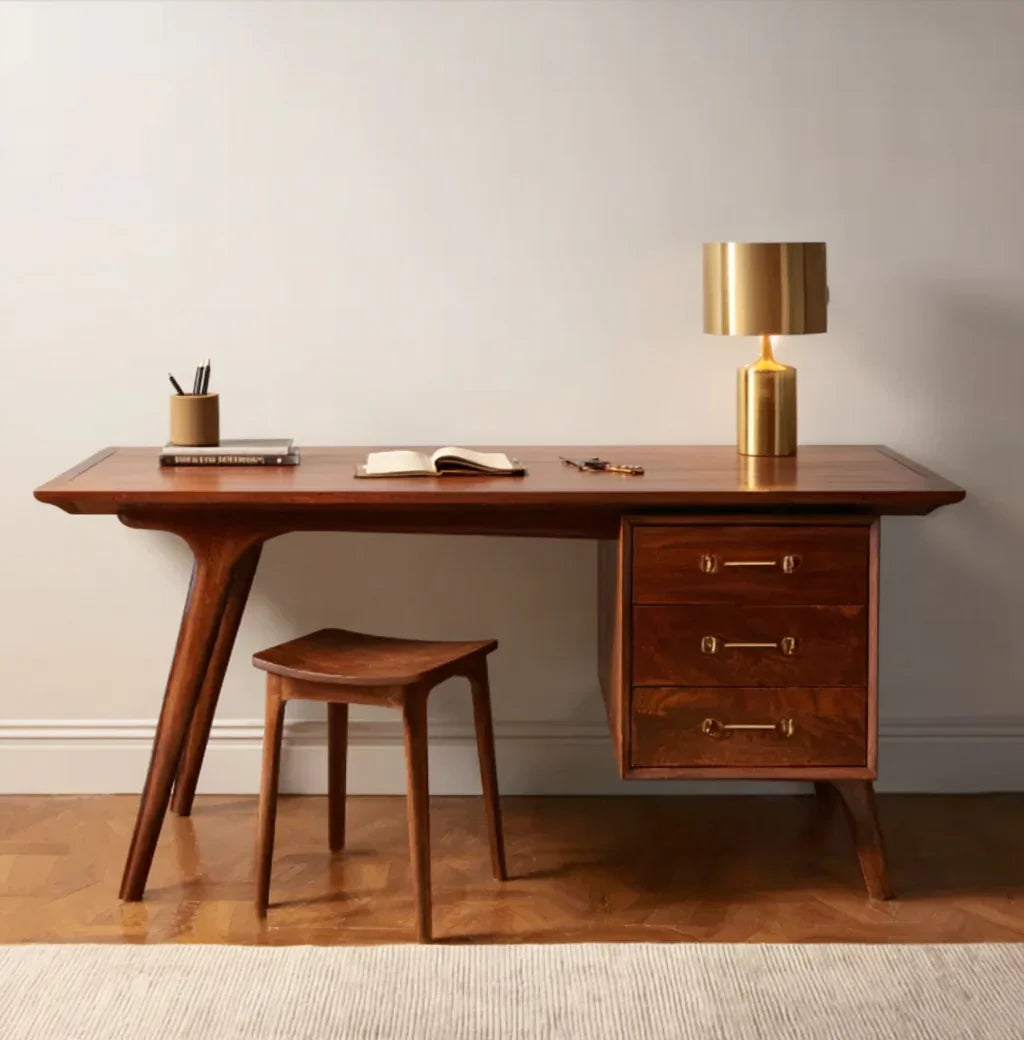 Mid-century modern wooden desk with matching stool, gold table lamp, open book, keys, and pencil holder