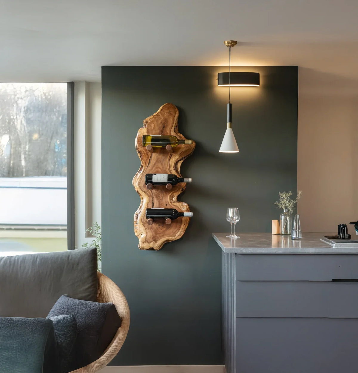 Modern living room with wooden wine rack holding bottles on dark gray wall, pendant light, and gray sofa