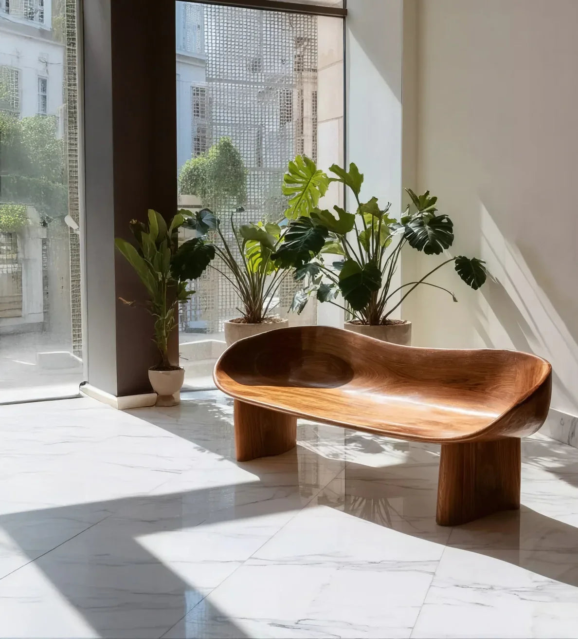 Curved wooden bench on marble floor with large green potted plants near glass windows