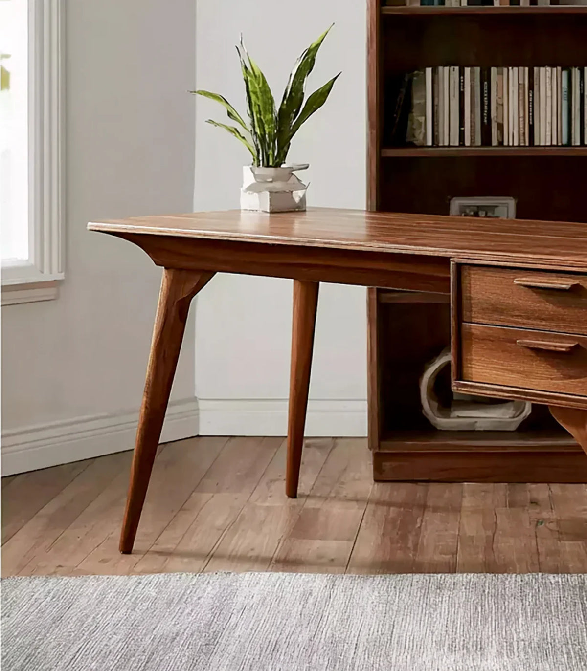Mid-century modern wooden desk with plant on top, hardwood floor, and bookshelf with books