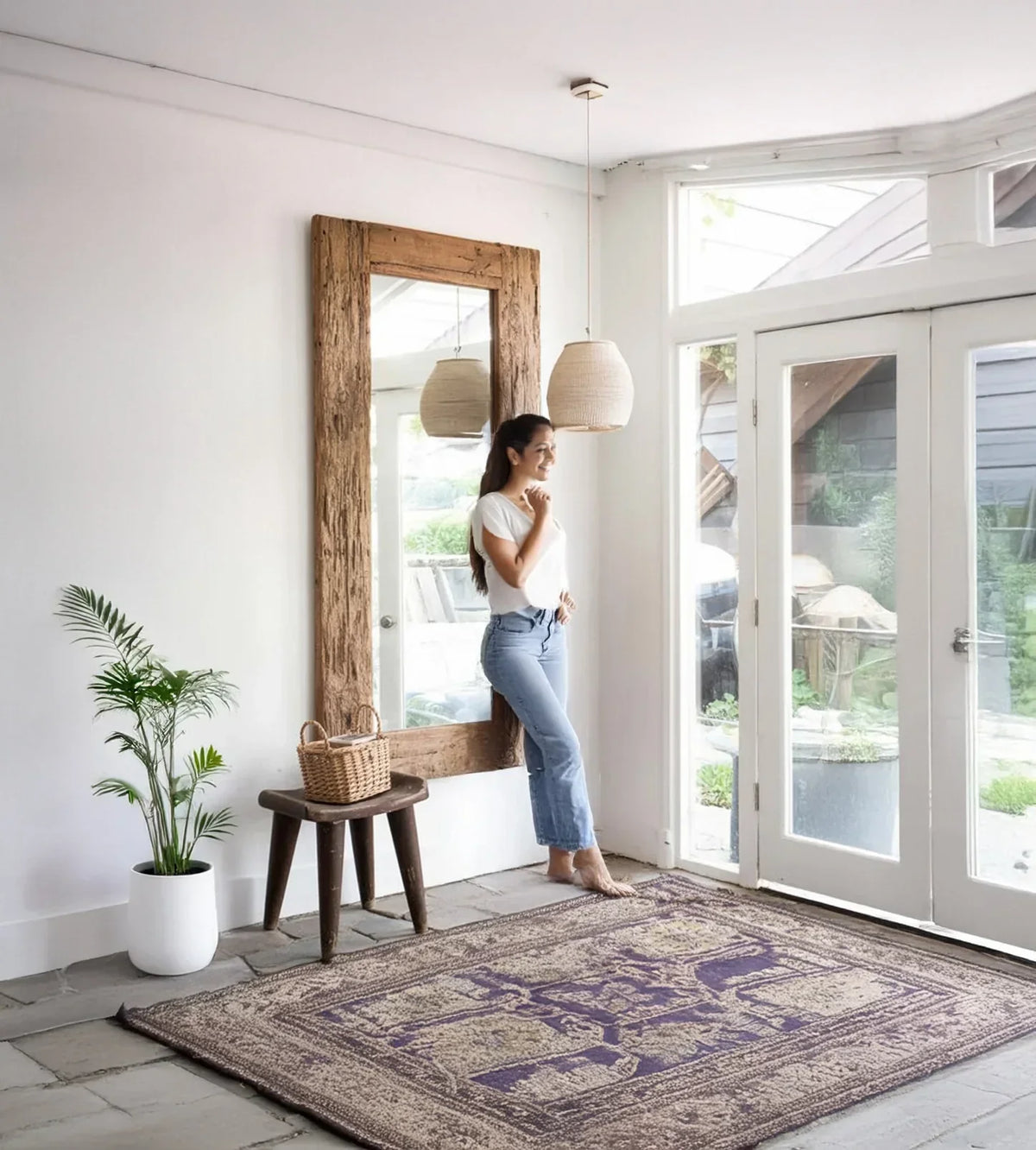 Bright entryway with large rustic wood-framed mirror, solid wood stool, potted plant, woven pendant lights, and decorative area rug.