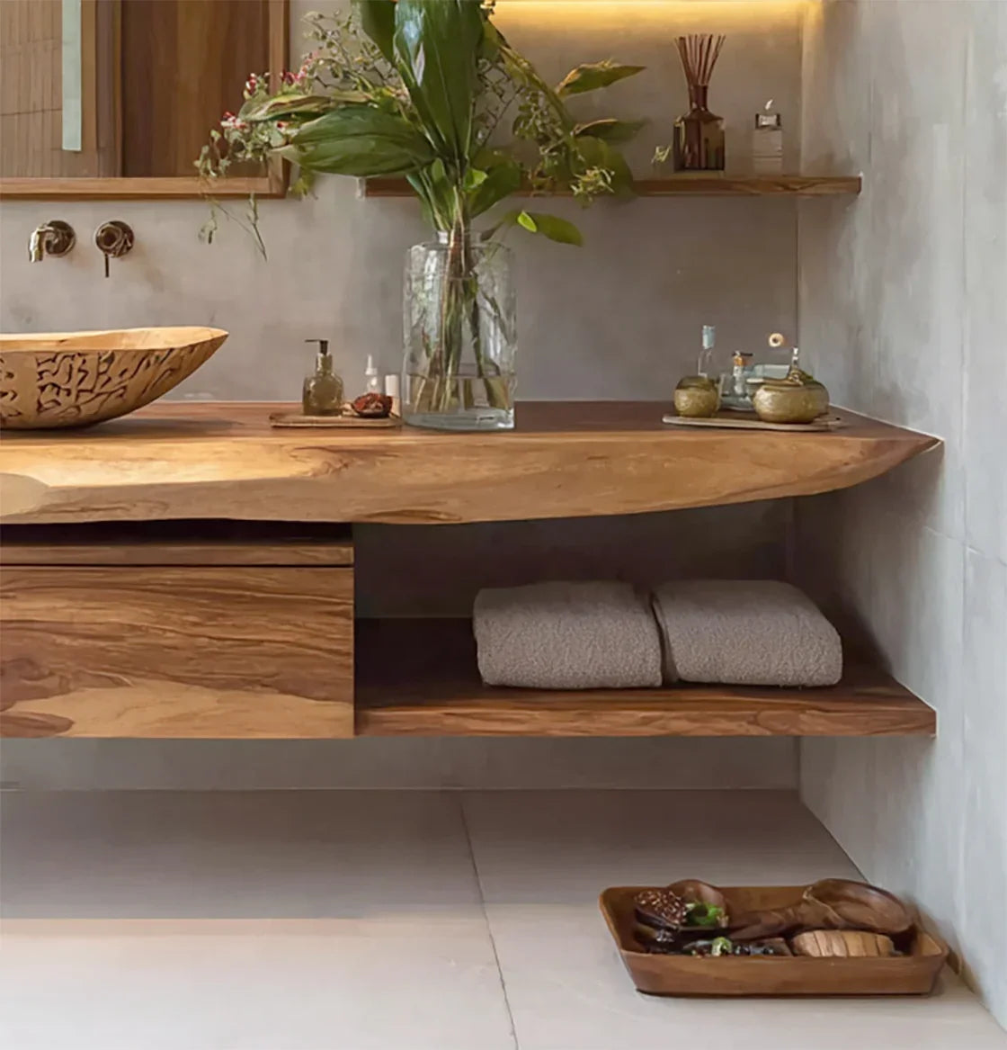 Modern bathroom with natural wood countertop, carved sink, glass vase with green plants, and wooden accessories