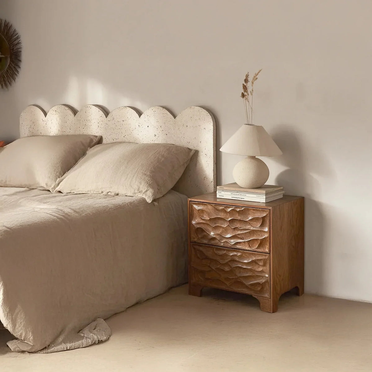 Solid wood sculpted nightstand beside bed with textured headboard in minimalist bedroom
