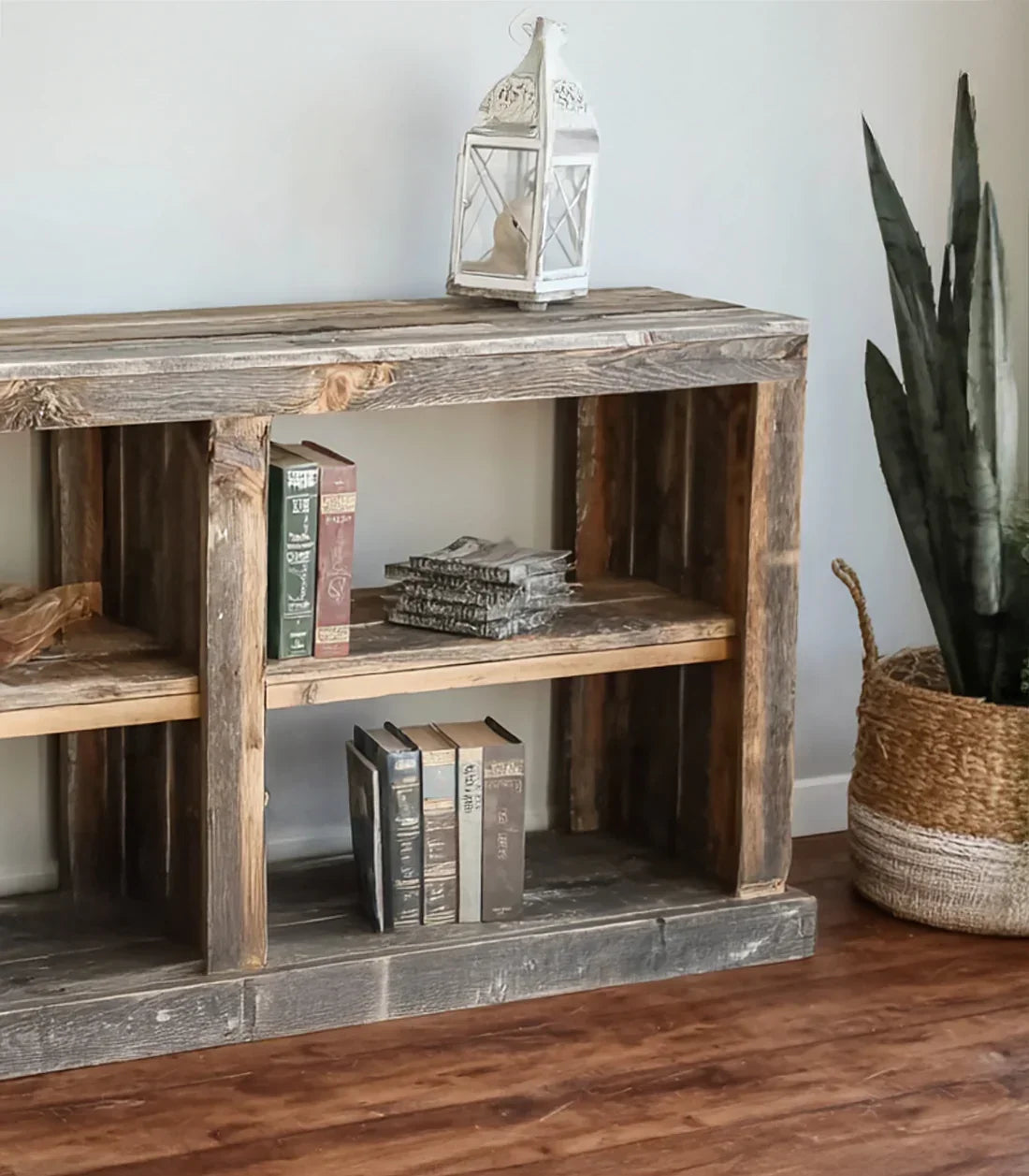Rustic solid wood bookshelf with books, lantern, and potted plant on hardwood floor
