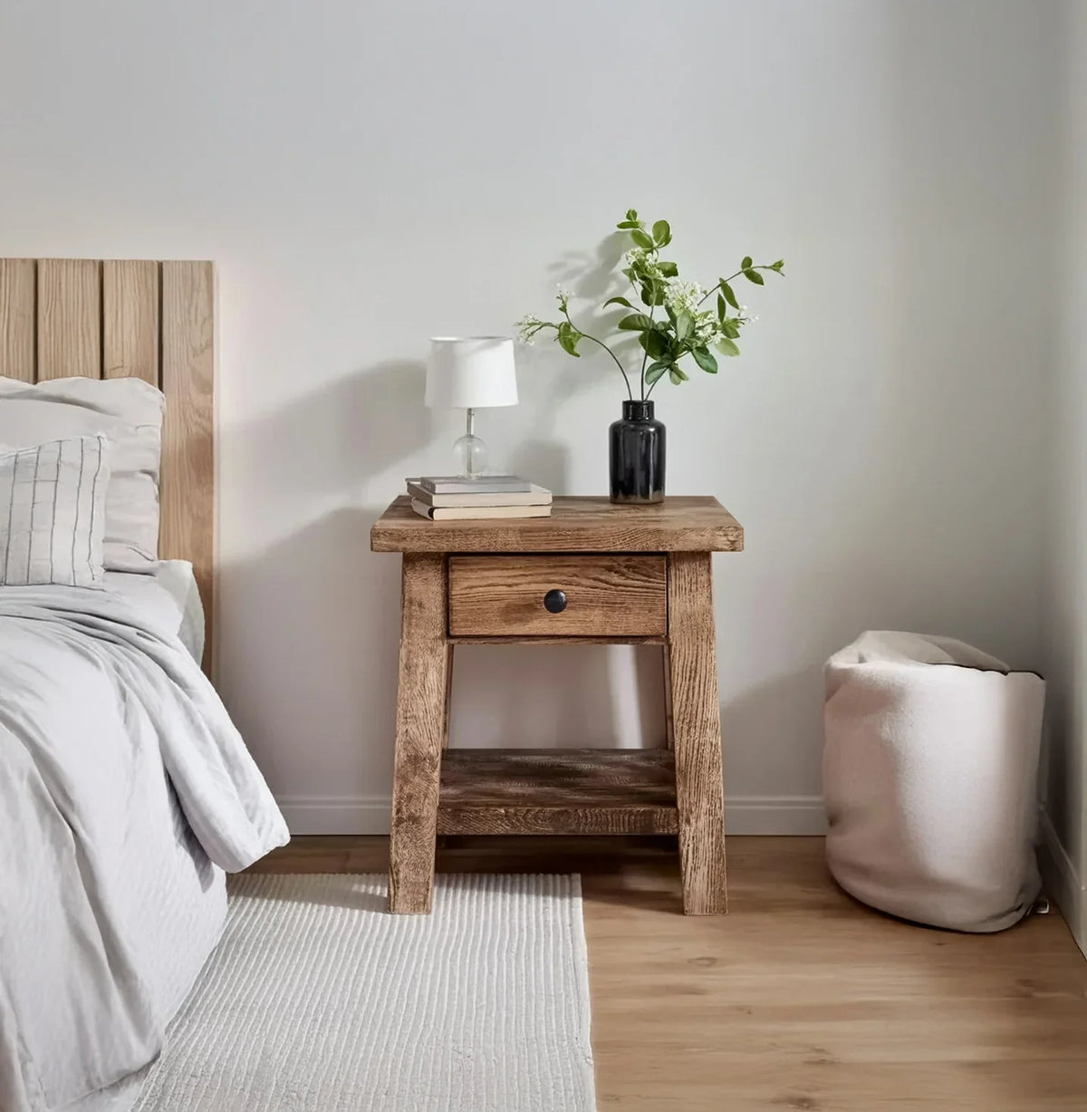 Rustic wooden nightstand with drawer, white lamp, books, and vase with green branches in modern bedroom