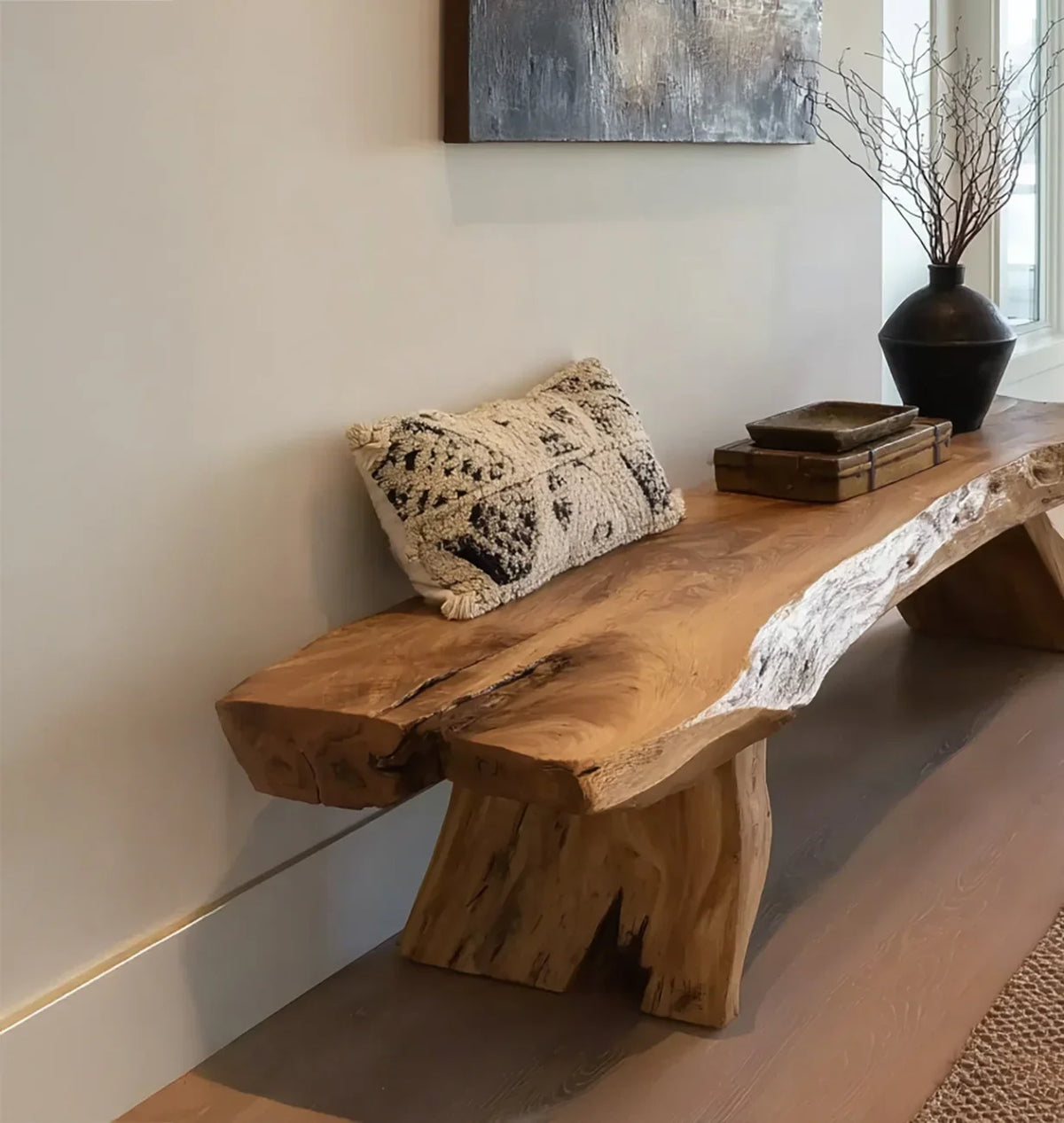 Live edge wooden bench with textured cushion, decorative books, ceramic bowl, and vase with branches in modern room